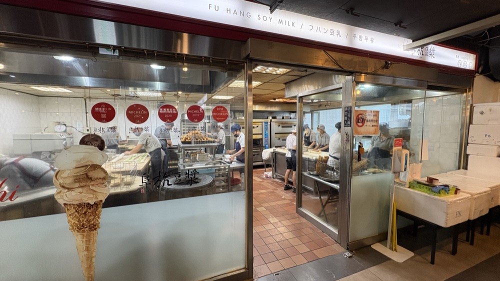 阜杭豆漿の厨房。ガラス越しに生地を伸ばす店員と、積まれた油條が見える