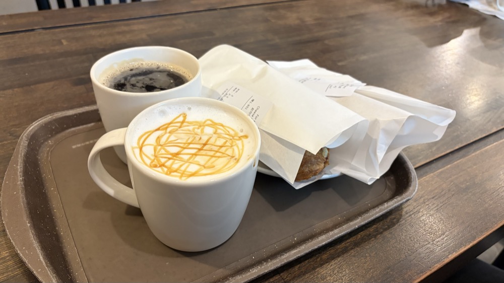 スターバックスのトレーに乗ったコーヒーとキャラメルソースのかかったラテ、紙に包まれたフード2つ