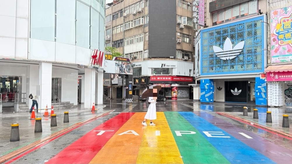 雨の西門町。虹色の横断歩道を傘をさして歩く妻