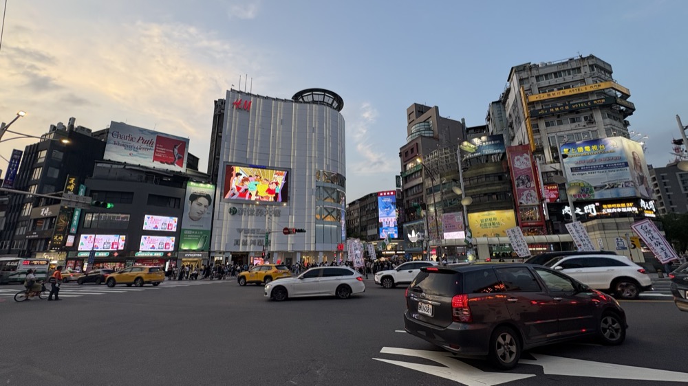 夕方の西門町の交差点。ビルの看板と行き交う車