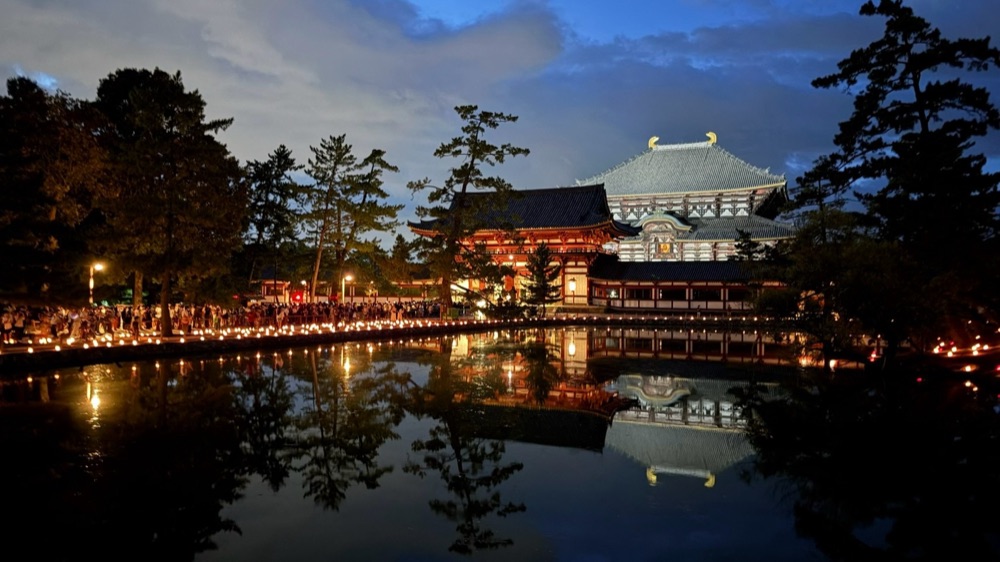 夜の東大寺。鏡池の水面にろうそくの灯りと大仏殿が映っている